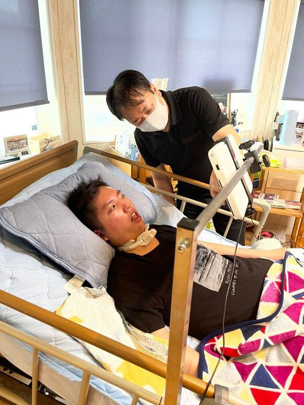 中1のとき交通事故に遭い、8年間、24時間介護を受けながら暮らしている菊池蒼磨さん（21）。現在、松尾さんが作った特殊なスイッチを使って会話補助機での入力を練習中だ（筆者撮影）