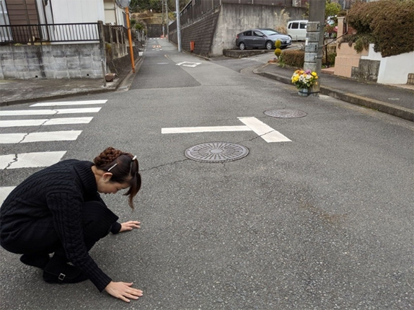 息子のマサムネくんが亡くなった事故現場で。「ここにまだ、自転車の擦過痕が残っているんです」とアスファルトをさする理絵さん（筆者撮影）