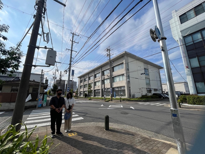 三重県津市の事故現場に佇む平田さん夫妻。晴琉くんは後方の横断歩道を横断中だった（筆者撮影）
